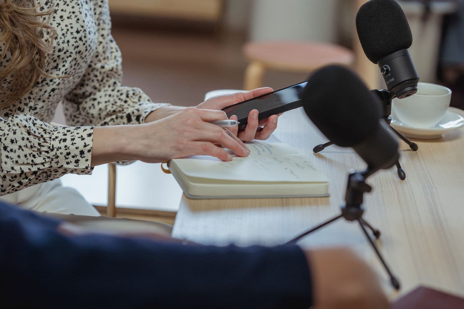 A researcher taking handwritten notes during a recorded research interview, with microphones on the table, before coding the transcript