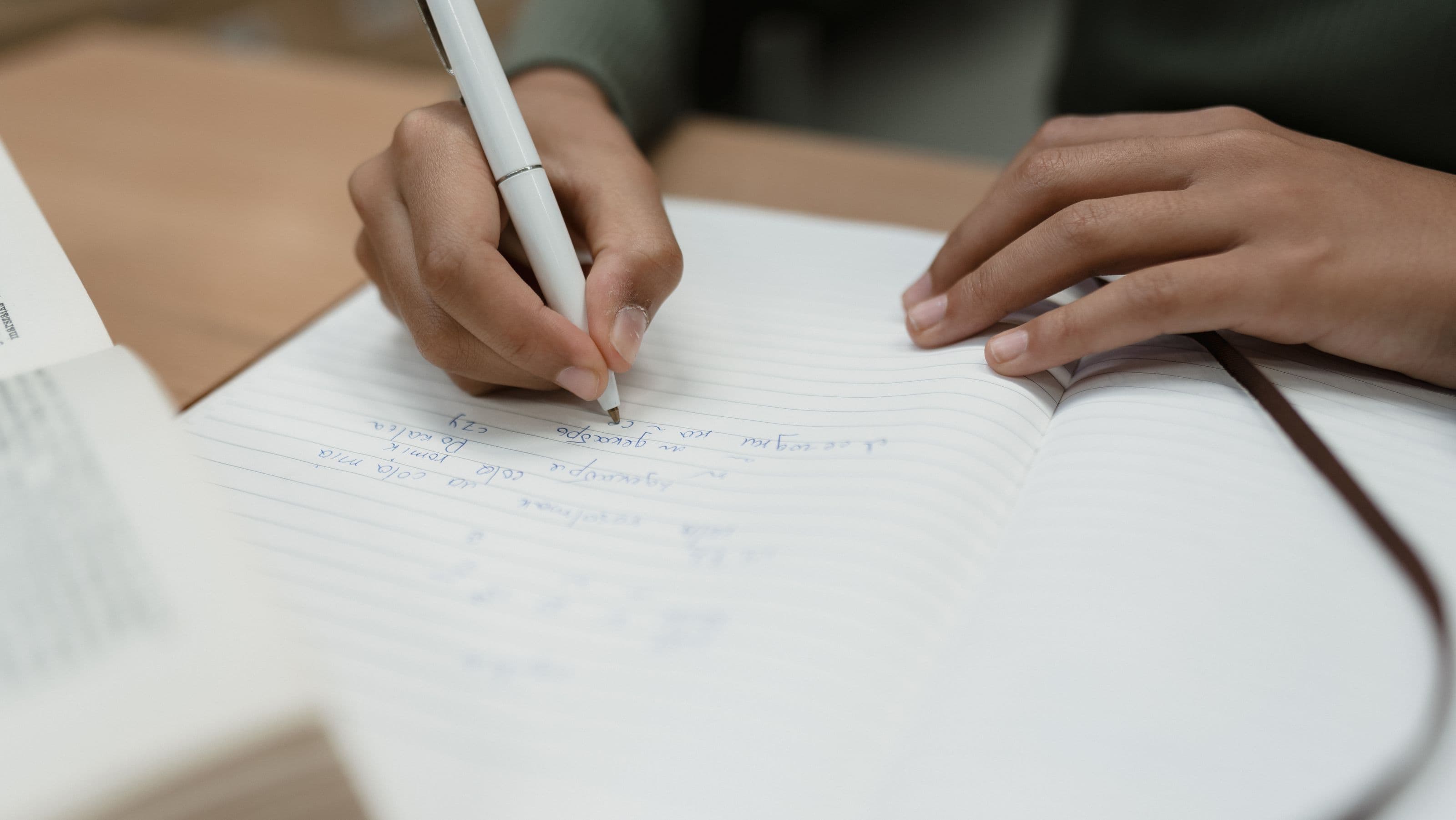 Close-up of a hand writing reflective notes in an open notebook