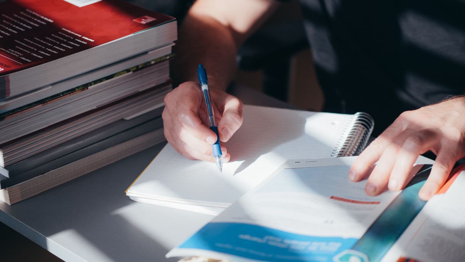 A student coding interview transcripts by hand in a notebook, with textbooks stacked beside them