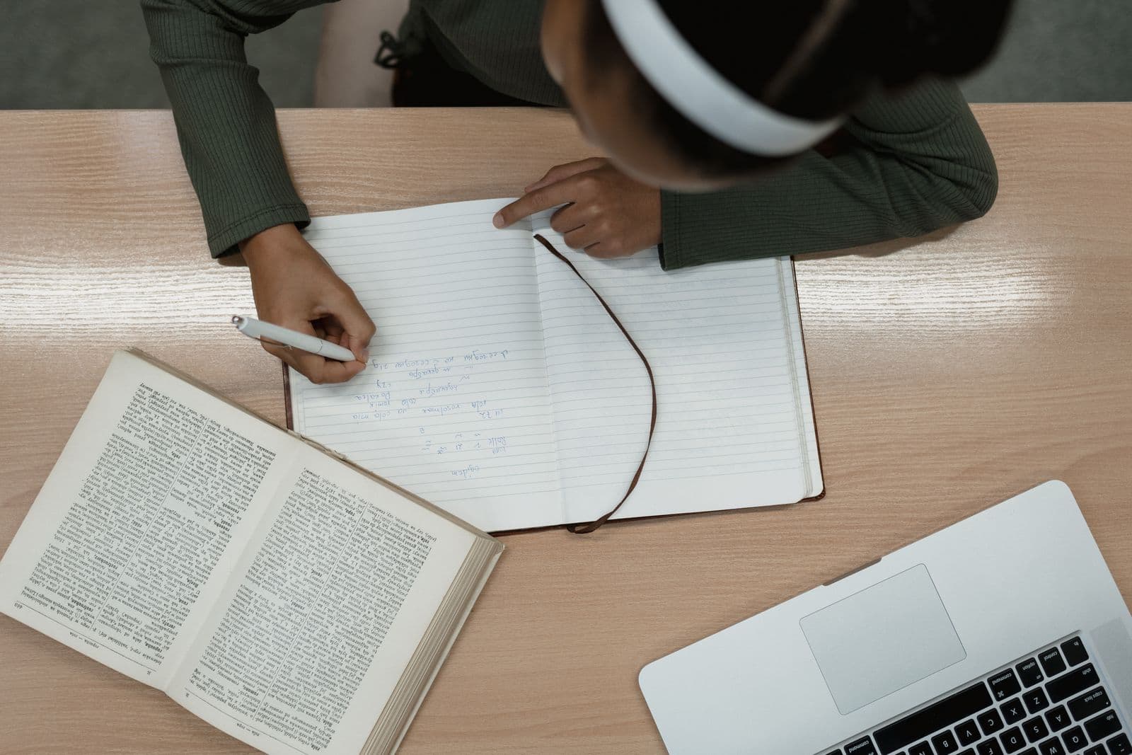 A researcher reviewing and synthesising academic literature with notebook and laptop at a library desk